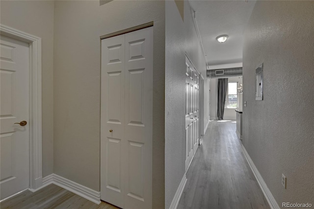 hallway featuring light wood finished floors, visible vents, baseboards, and a textured wall