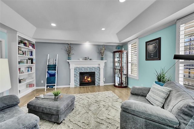 living room with a stone fireplace, light hardwood / wood-style flooring, built in features, and a raised ceiling