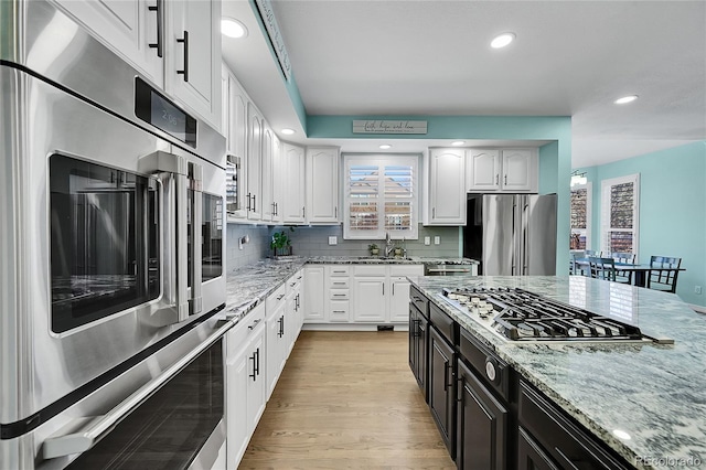 kitchen with appliances with stainless steel finishes, backsplash, white cabinets, light stone counters, and light wood-type flooring