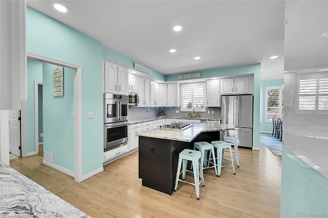 kitchen featuring a breakfast bar, stainless steel appliances, white cabinets, a kitchen island, and light wood-type flooring