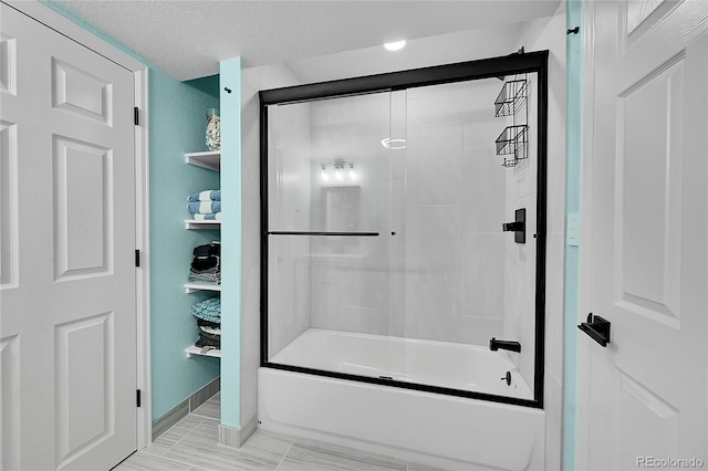 bathroom featuring a textured ceiling and combined bath / shower with glass door