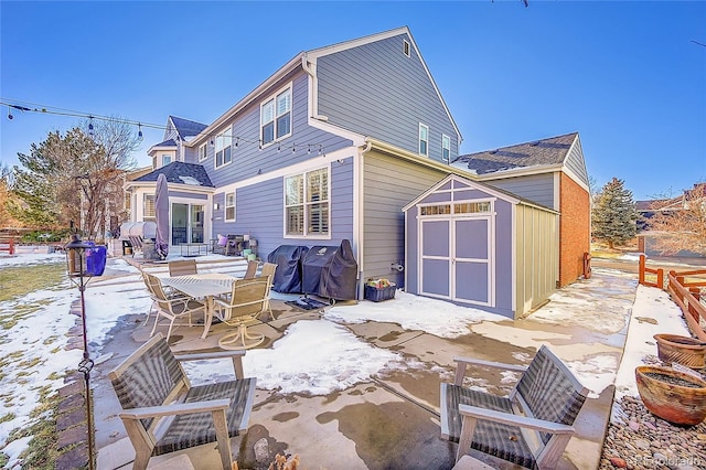 snow covered rear of property with a patio and a storage unit