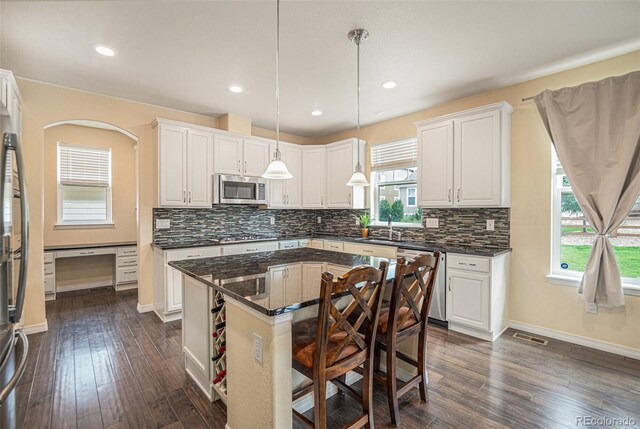 kitchen featuring appliances with stainless steel finishes, a kitchen island, white cabinetry, and decorative light fixtures