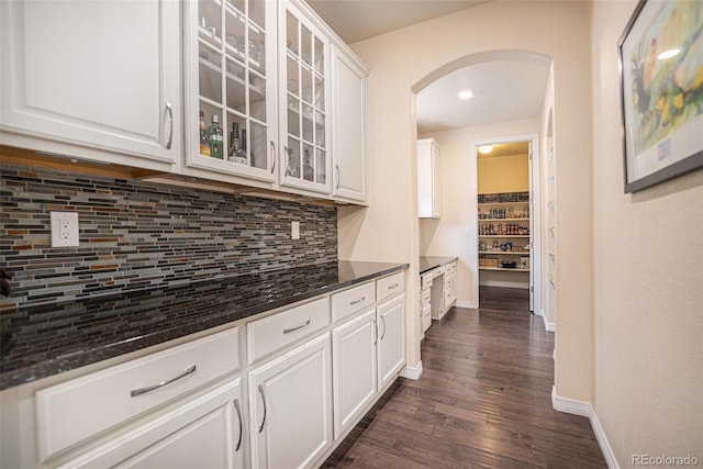 kitchen featuring dark wood-style floors, arched walkways, backsplash, glass insert cabinets, and white cabinetry