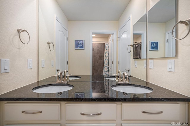 full bathroom with a tile shower, double vanity, and a sink