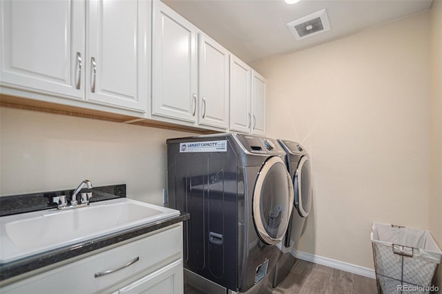 laundry area featuring wood finished floors, a sink, visible vents, washer and dryer, and cabinet space