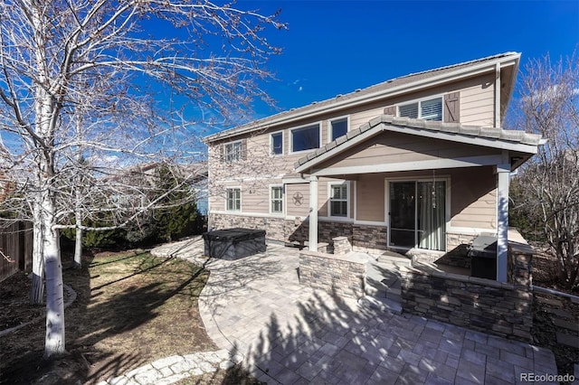 back of property featuring stone siding, a patio, and a covered hot tub