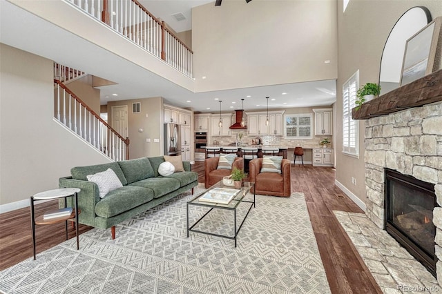 living room with light wood finished floors, visible vents, baseboards, stairway, and a stone fireplace