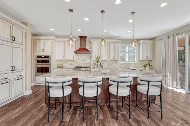 kitchen with wall chimney exhaust hood, appliances with stainless steel finishes, dark wood-type flooring, a center island, and light stone countertops