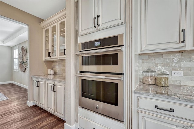 kitchen with dark wood-style floors, light countertops, double oven, glass insert cabinets, and baseboards