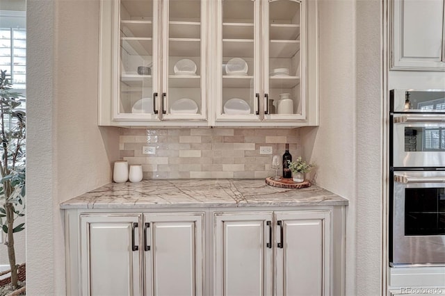 bar featuring a textured wall, tasteful backsplash, and stainless steel double oven