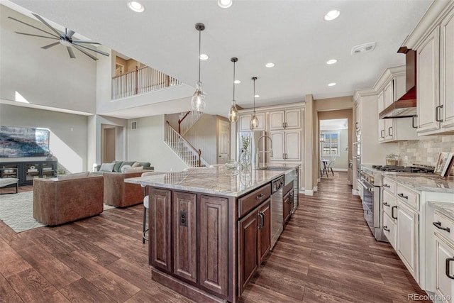 kitchen with dark wood-style floors, a breakfast bar area, appliances with stainless steel finishes, open floor plan, and wall chimney range hood