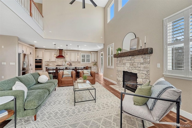 living room featuring recessed lighting, ceiling fan, a stone fireplace, light wood-type flooring, and baseboards