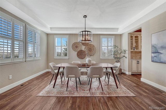 dining space with visible vents, baseboards, dark wood finished floors, and a tray ceiling