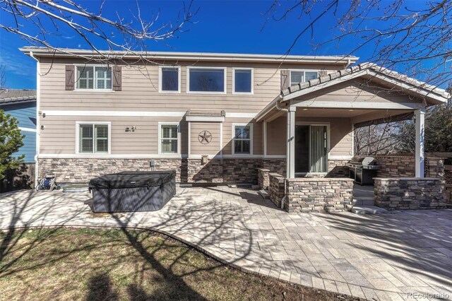 rear view of property featuring stone siding and a patio area