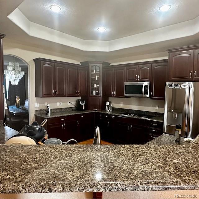13291 N Harback Rd, Bennett, CO 80102 - kitchen featuring appliances with stainless steel finishes, a raised ceiling, dark brown cabinetry, a chandelier, and recessed lighting