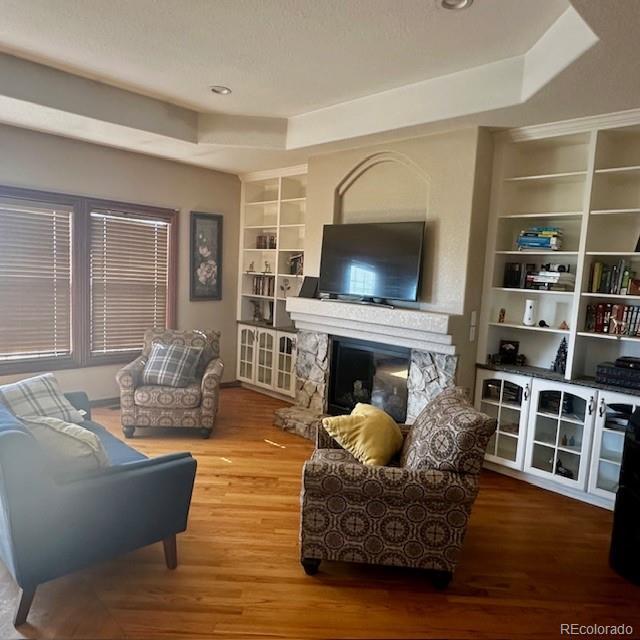 13291 N Harback Rd, Bennett, CO 80102 - living area featuring built in features, wood finished floors, a tray ceiling, and a stone fireplace