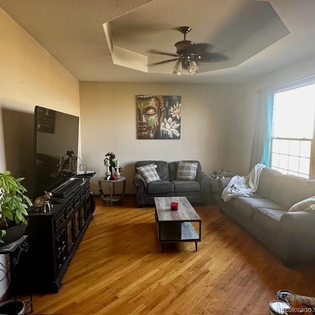 13291 N Harback Rd, Bennett, CO 80102 - living area with light wood finished floors, a tray ceiling, and ceiling fan