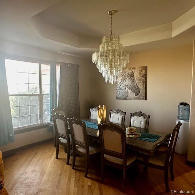 13291 N Harback Rd, Bennett, CO 80102 - dining room with a tray ceiling, wood finished floors, and a chandelier