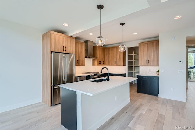 kitchen with pendant lighting, high end refrigerator, a center island with sink, sink, and wall chimney exhaust hood