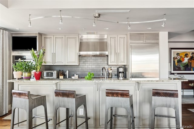 bar with built in fridge, extractor fan, white cabinetry, backsplash, and light stone countertops