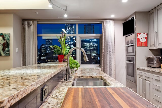 kitchen with double oven, a sink, gray cabinetry, and light stone countertops