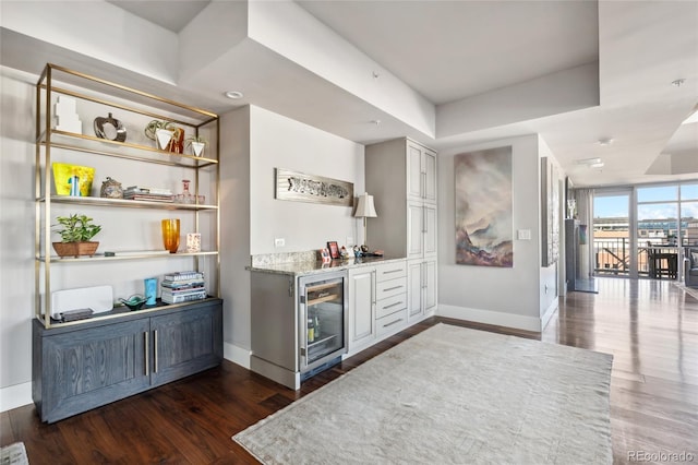 bar with a tray ceiling, dark wood finished floors, a bar, beverage cooler, and baseboards