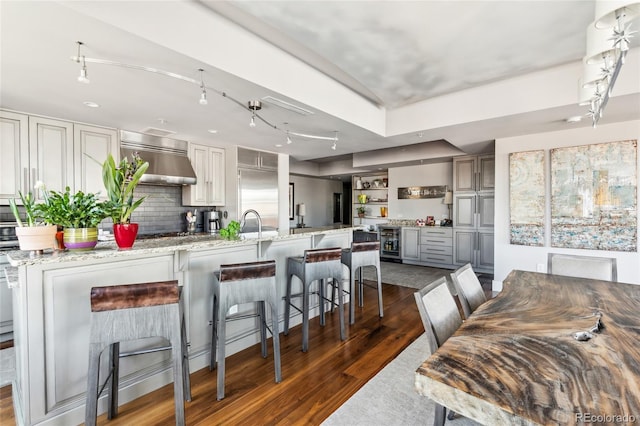 kitchen with dark wood finished floors, decorative backsplash, light stone counters, gray cabinetry, and wall chimney range hood