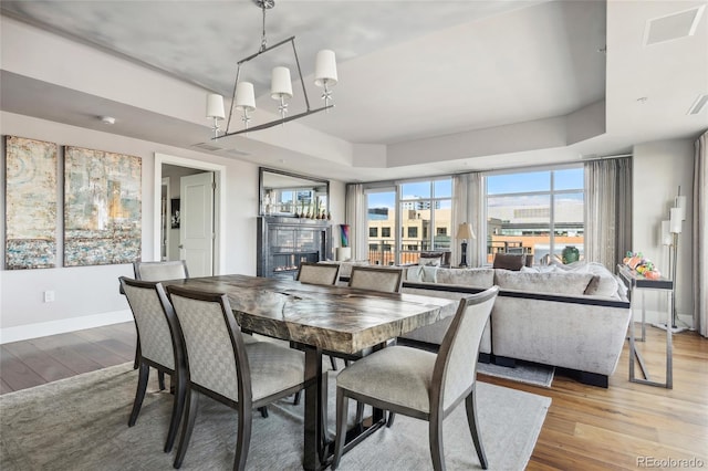 dining room featuring a chandelier, a tray ceiling, light wood finished floors, and baseboards