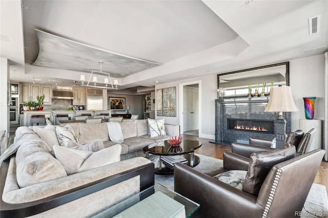 living area with baseboards, visible vents, a glass covered fireplace, wood finished floors, and a tray ceiling