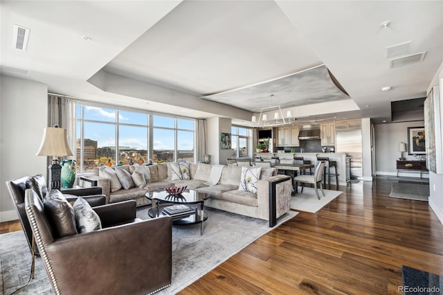 living area with a tray ceiling, dark wood-type flooring, visible vents, and baseboards