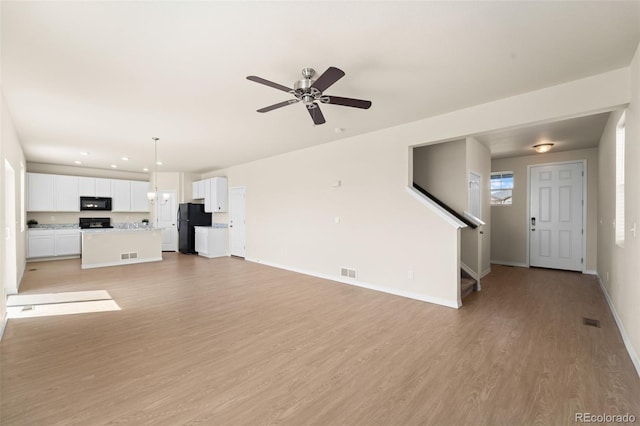 unfurnished living room featuring stairs, light wood finished floors, visible vents, and ceiling fan
