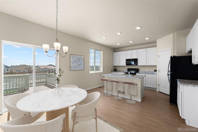 kitchen featuring baseboards, light wood-style flooring, white cabinets, a kitchen island with sink, and black appliances