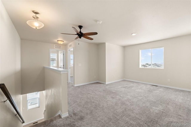 empty room with light colored carpet, baseboards, a ceiling fan, and visible vents