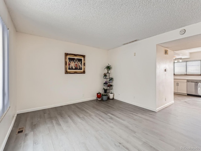 empty room with a textured ceiling and light hardwood / wood-style flooring