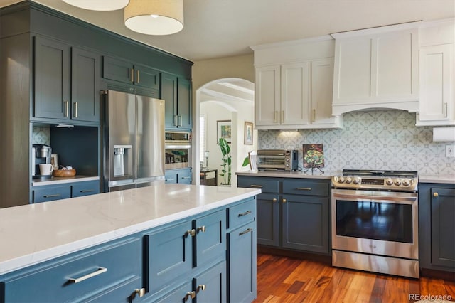 7289 Stroh Rd, Parker, CO 80134 - kitchen with stainless steel appliances, arched walkways, backsplash, dark wood-style flooring, and white cabinetry