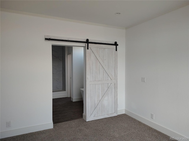 unfurnished bedroom featuring ornamental molding, a barn door, and dark colored carpet