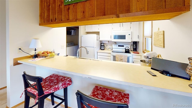 kitchen featuring sink, white cabinetry, kitchen peninsula, white appliances, and washer and clothes dryer