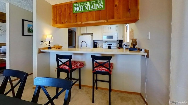 kitchen featuring white appliances, a breakfast bar, white cabinets, light carpet, and kitchen peninsula