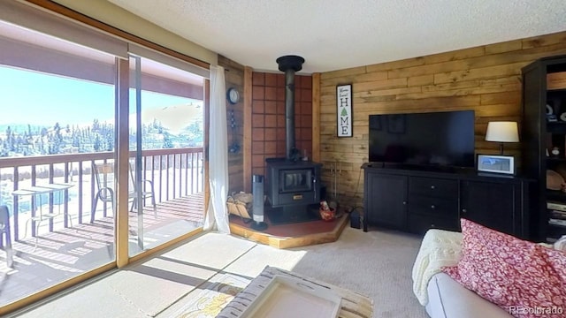 living room with carpet flooring, wood walls, a textured ceiling, and a wood stove