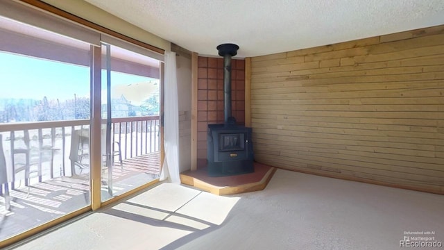 unfurnished living room featuring wood walls, a textured ceiling, and a wood stove