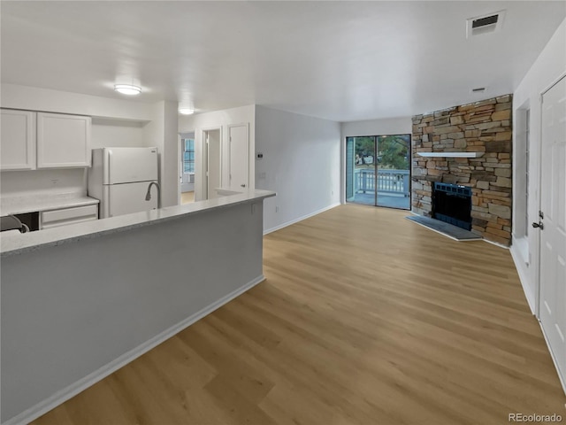 kitchen with white cabinets, light wood-type flooring, white fridge, and a fireplace