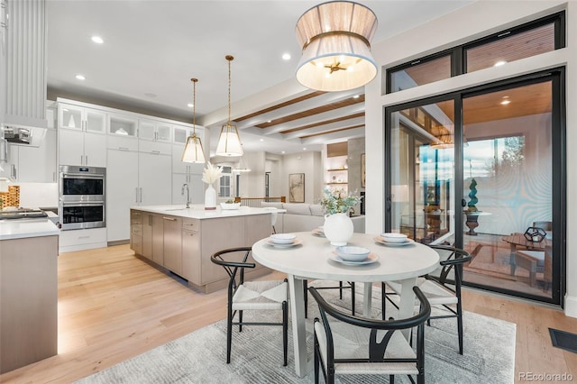 dining space with a chandelier, light hardwood / wood-style floors, beamed ceiling, and sink