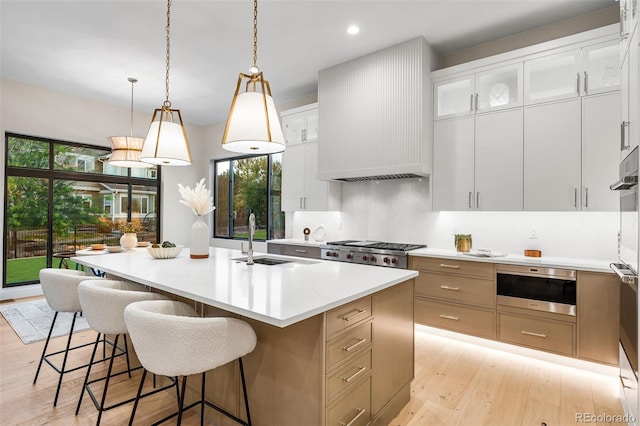 kitchen with decorative light fixtures, a kitchen island with sink, white cabinets, custom range hood, and light wood-type flooring