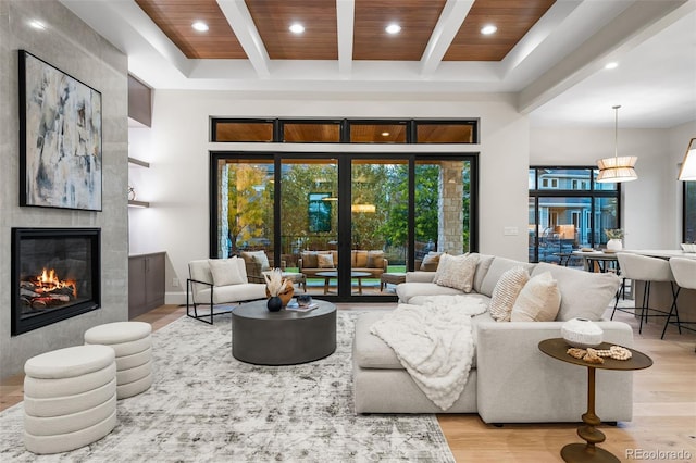 living room with a tiled fireplace, beamed ceiling, wooden ceiling, and light wood-type flooring