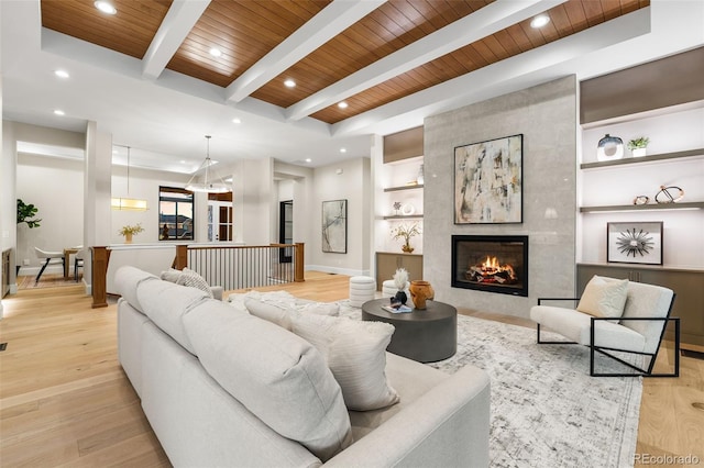 living room featuring beam ceiling, built in features, a tile fireplace, and wooden ceiling