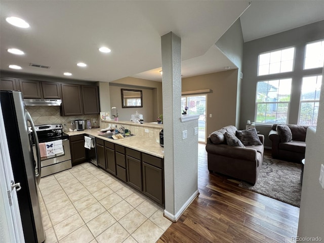 kitchen with light wood-type flooring, backsplash, dark brown cabinets, and appliances with stainless steel finishes