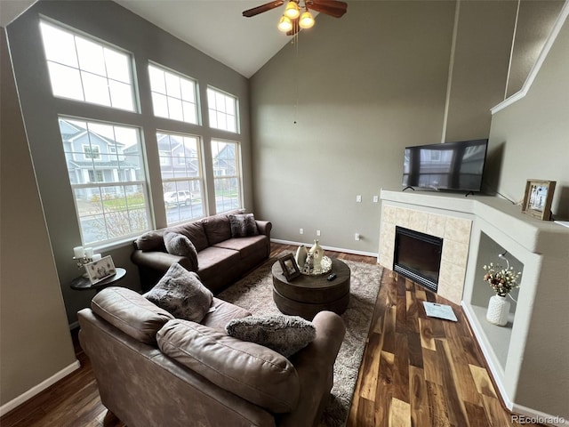 living room with a tiled fireplace, dark wood-type flooring, high vaulted ceiling, and ceiling fan