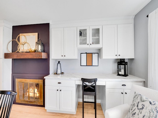 kitchen featuring light stone counters, built in desk, light hardwood / wood-style floors, and white cabinets