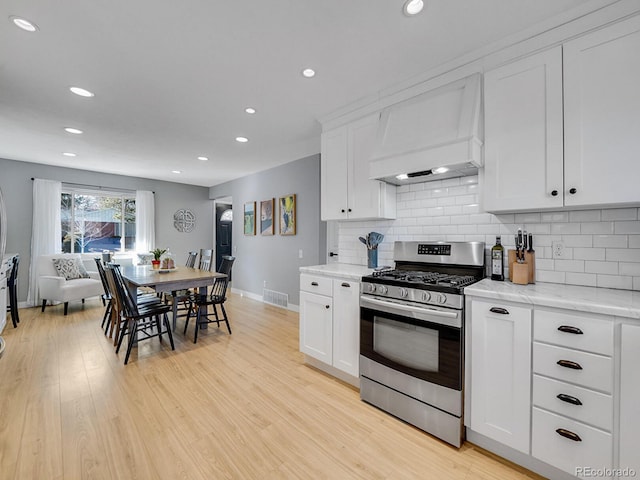 kitchen with stainless steel gas range, light hardwood / wood-style floors, custom range hood, and white cabinets